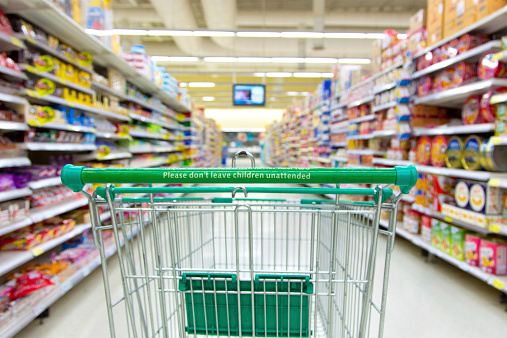 A shopping cart by a store shelf in a supermarket