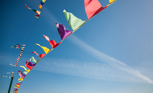 Multicolored flags against the blue sky with traces from planes