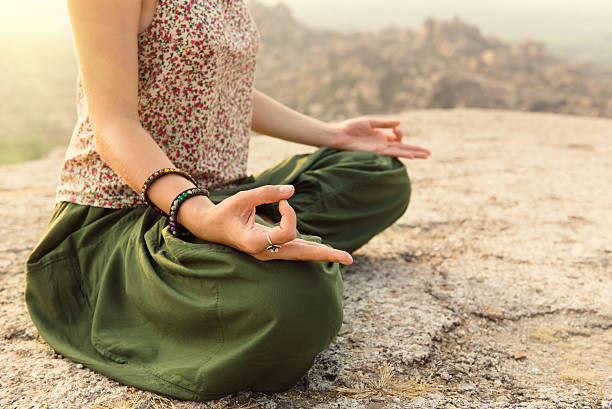 Young female athlete exercising Yoga in Lotus position during summer day by the rock formation. Copy space.
