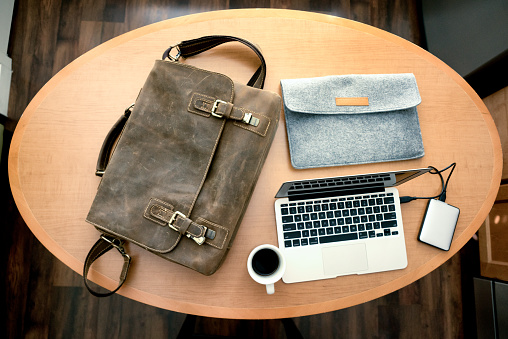 Laptop case with notebook computer and an external hard drive with a felt laptop sleeve and a cup of coffee looking down on an oval table.