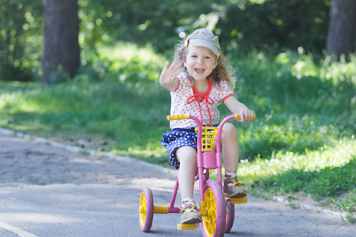 Two year-old laughing girl is wearing corduroy flat cap and polka-dotted costume cycling kids pink and yellow tricycle