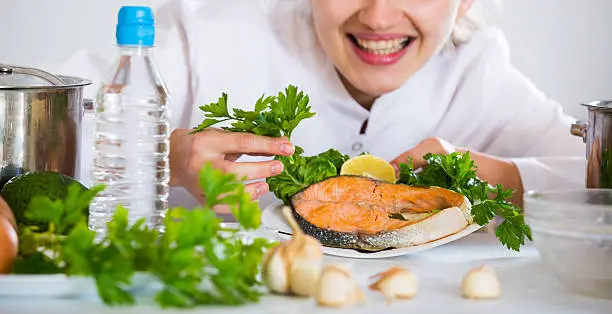 Positive female chef posing with trout fillet in kitchen