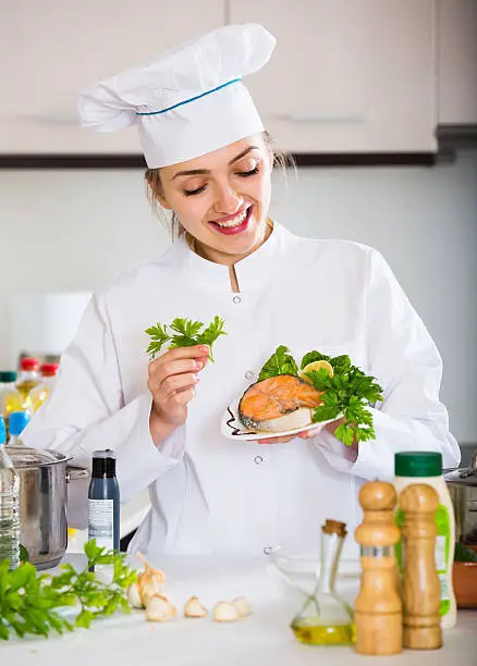 Positive female chef posing with trout fillet in kitchen