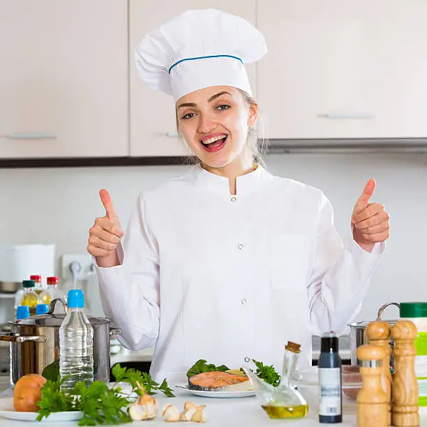 Positive female chef posing with trout fillet in kitchen
