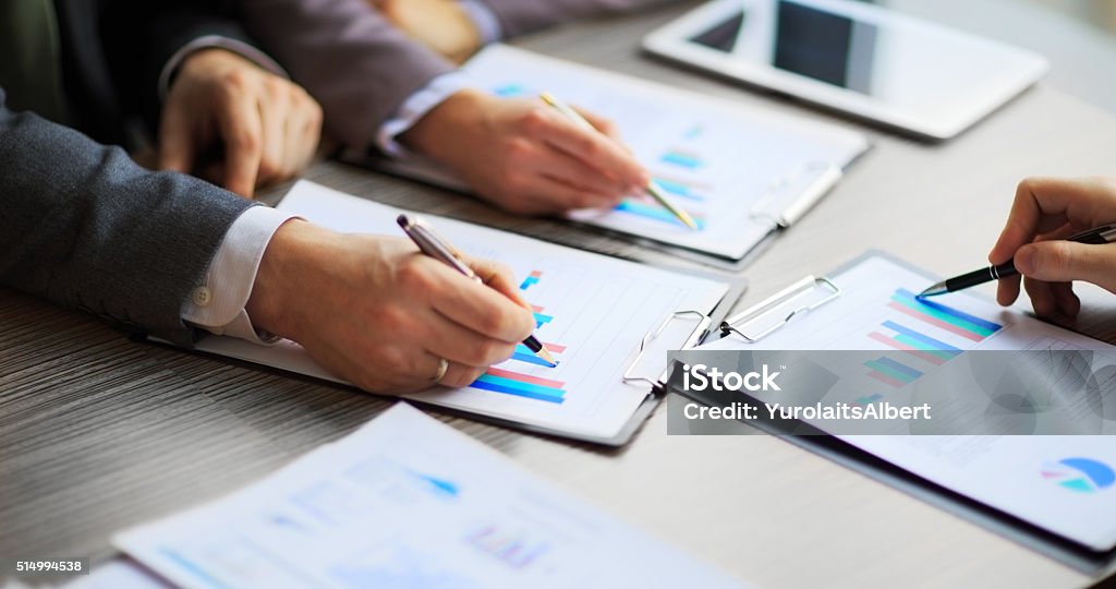 Discussing the scheme. Discussing the scheme. Side view of business people, pointing handles on the chart together, sitting at the table Business Stock Photo