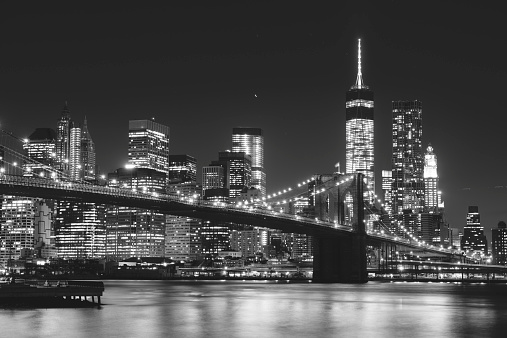 Night at Brooklyn bridge with illuminating buildings from Manhattan in background. New York City, US. Black and White image. 