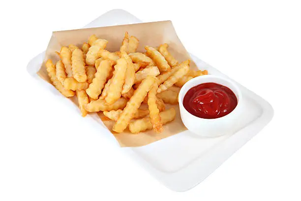 Slices of French fries with a cup of tomato ketchup, lie on parchment in a white rectangular plate, studio shot, isolated on white background.
