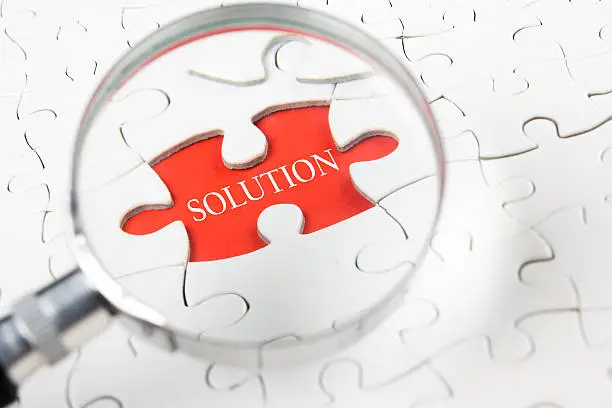 Photo of Solution word with hand holding magnifying glass over jigsaw puzzle