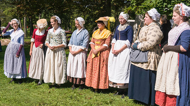 Women in colonial dress of the 18th century Wheaton, IL, USA - September 13, 2014: A group of unidentified women in period dress stand listening to a speaker off camera as they give a presentation of colonial lifestyles and attire in 18th-century America at a reenactment of the American Revolutionary War (1775-1783). historical reenactment stock pictures, royalty-free photos & images