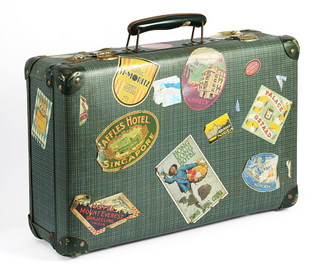 Old vintage suitcase covered with colorful travel labels depicting a range of international tourist destinations conceptual of travel and vacations isolated on white