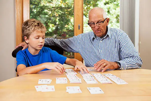 A grandfather, in his 70s is teaching his 10 year old grandson the playing card game Solitaire.