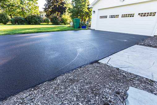 A fresh blacktop resealing job just finished on this asphalt driveway in a suburban residential district.