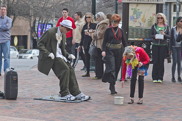 Living Statue Street Artist Asheville, North Carolina, USA - March 2, 2014: Living statue street artist showing a man in a suit being blown backward and leaning at an impossible angle as a woman bends in costume over to give him a tip and a crowd of people watch on March 2, 2014 in downtown Asheville, NC person falling backwards stock pictures, royalty-free photos & images