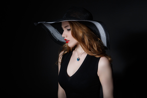 Beautiful Woman in big black hat on dark background