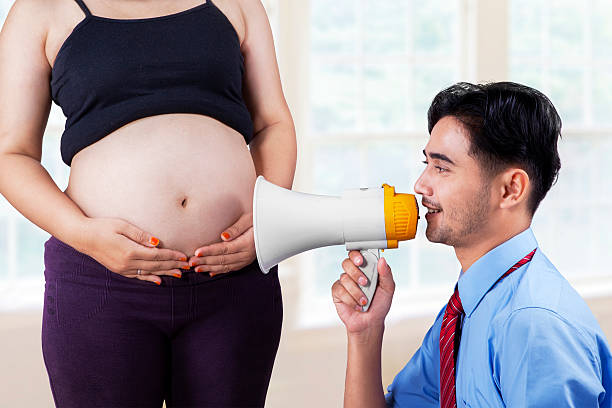 Husband talking to his baby on his wife's belly with megaphone, shot at home