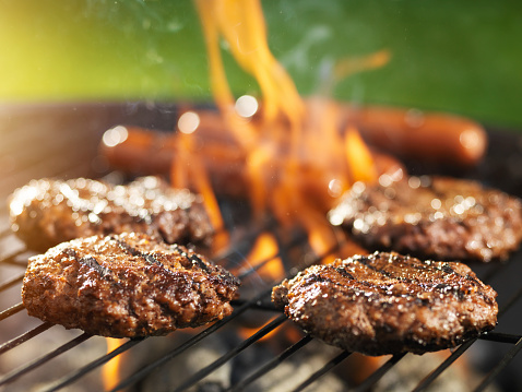 hamburgers and hotdogs cooking on flaming grill shot with selective focus