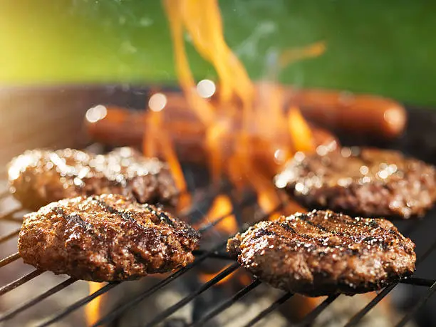 Photo of hamburgers and hotdogs cooking on flaming grill