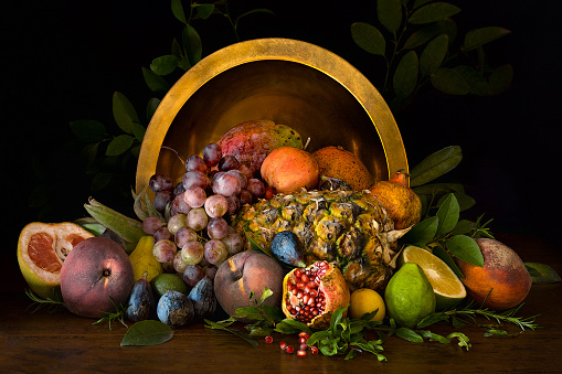 Assorted summer fruit displayed on a tabletop in front of a large brass bowl against a dark background.
