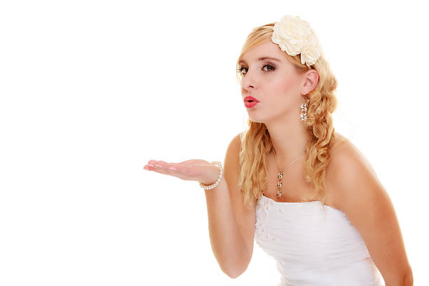 Wedding day. Portrait of young blond woman romantic attractive bride blowing a kiss or showing blank copy space on empty hand isolated on white. Studio shot.