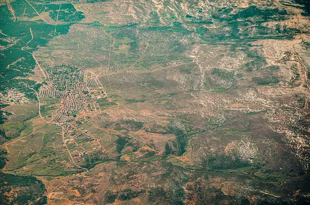 Village seen from above at the left of the frame. In the resembling satellite image, snow is distinguished at the right on the terrain. Green