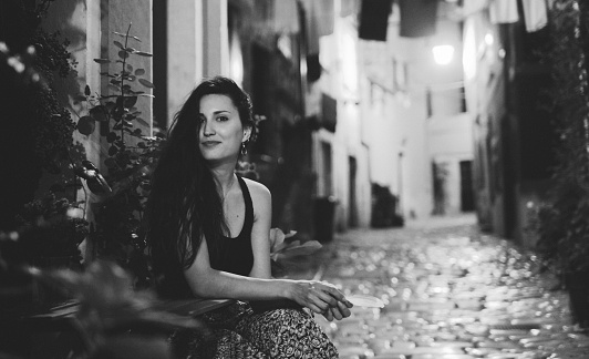 Black and white portrait of a young fashionable brunette relaxing in the old town of Rovigno, Istria, Croatia. She is just outside her apartment in the Old town, enjoying the quiet summertime evening in town. Shot in letterbox aspect ratio for more horizontal copy space.