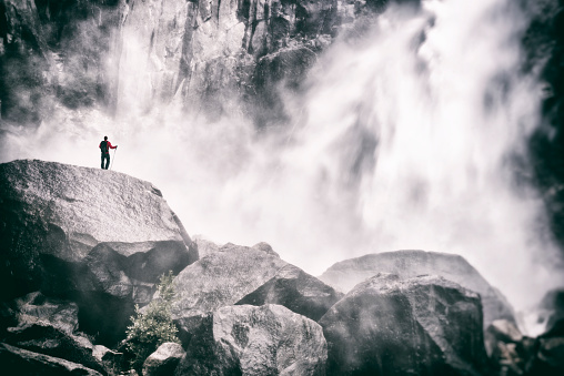 A man exploring the base of a huge waterfall 