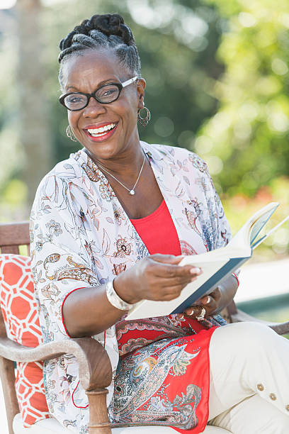 madura mulher afro-americana sentada ao ar livre, leitura - woman with glasses reading a book imagens e fotografias de stock