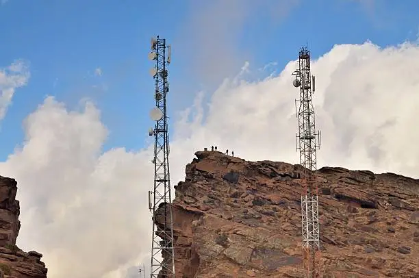 Tourist have climbed up a mountain behind some microwave antennas at Oukameden, Morocco and are silhouetted against the cumulus clouds in a blue sky