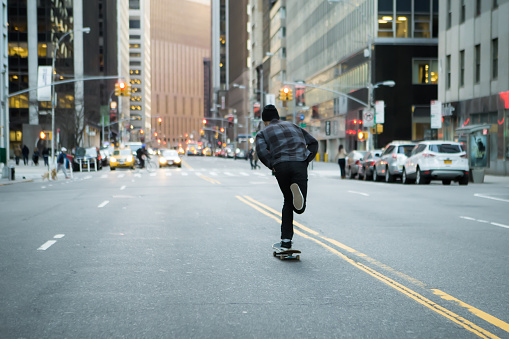 Back figure of young skateboarder cruising donw the city street before sunset. Photographed in New York City in Feb 2016.
