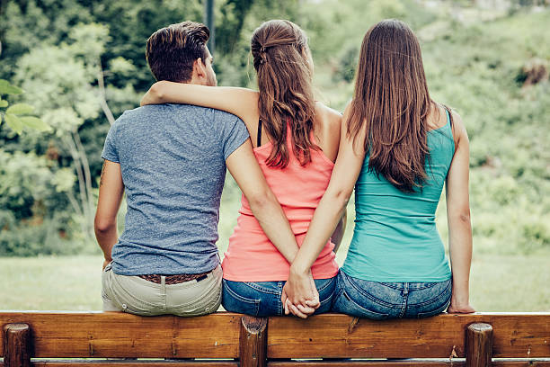 Love triangle Love triangle, a girl is hugging a guy and he is holding hands with another girl, they are sitting together on a bench infidelity photos stock pictures, royalty-free photos & images