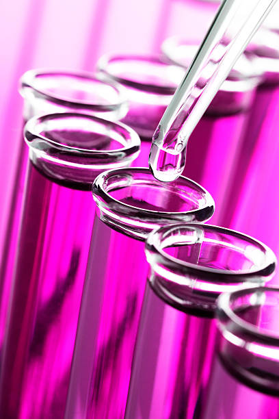 This is a close up photo of test tubes with a pipette dropping liquid into one of the tubes. The focus is on the drop of liquid and drops off quickly.