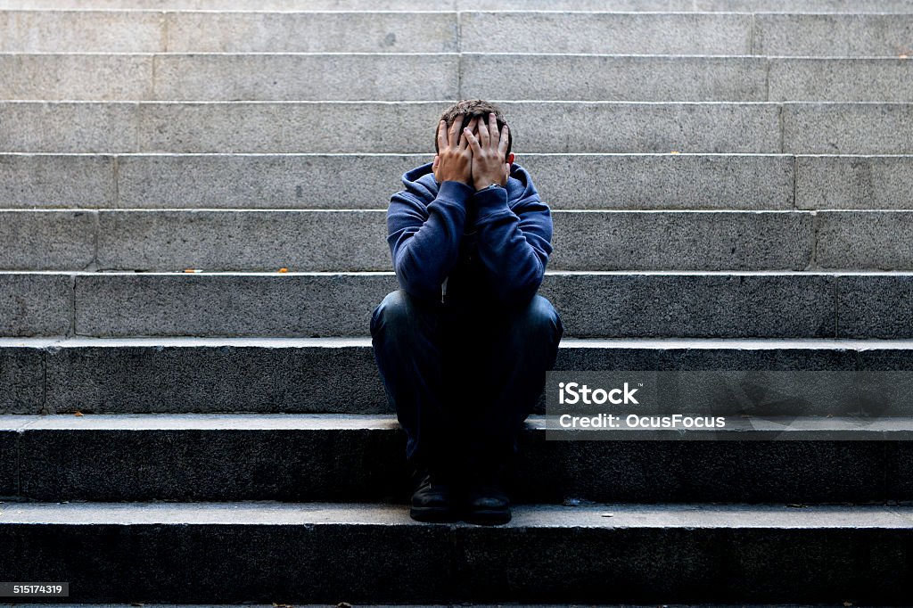 Young man suffering depression sitting on ground street concrete stairs Young desperate man in casual clothes abandoned lost in depression sitting on ground street concrete stairs alone suffering emotional pain, sadness, looking sick in grunge lighting Unemployment Stock Photo
