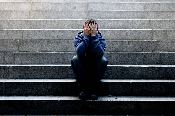 Young man suffering depression sitting on ground street concrete stairs stock photo