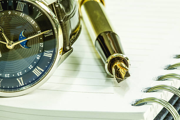 istock Gold fountain pen on blank notepad and watch 515192962