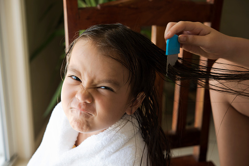 a girl is upset face, her  mother do head lice treatment.