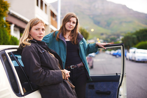 Portrait of two young friends standing beside their car on the street