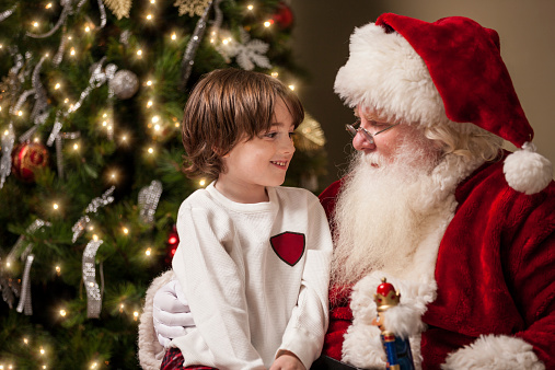 Funny kid with a smile on his face in a red hat Santa holds Christmas gift in his hand. Happy Baby in Santa Red Hat Keeps Christmas Presents