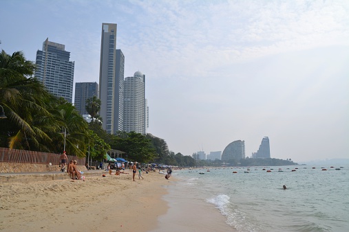 Pattaya, Thailand - December 30, 2013: tourists relaxing and sunbathing at Nakluea beach, surrounded by high rise apartment buildings