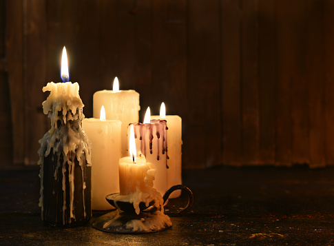 Group of evil candles burning in the darkness and copy space on wooden background. Black magic ritual or scary halloween rite.