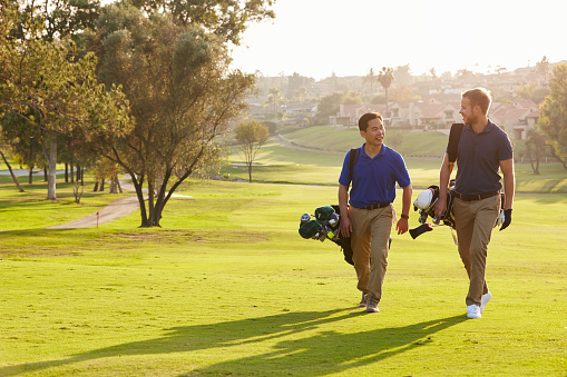 Two Male Golfers Walking Along Fairway Carrying Bags