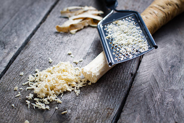 Grated horseradish root with grater on wooden gray table. Grated horseradish root with grater on wooden gray table. horseradish stock pictures, royalty-free photos & images