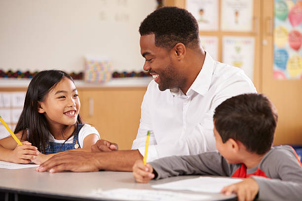 istock Teacher sitting at desk with two elementary school pupils 515262252