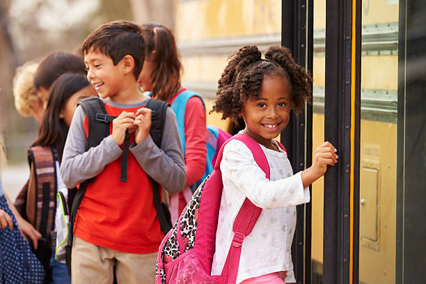 escola primária de rapariga na frente do autocarro escolar na fila - school bus imagens e fotografias de stock
