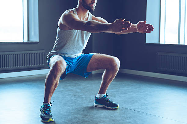 Deep squat. Part of young man in sportswear doing squat at gym squatting position photos stock pictures, royalty-free photos & images