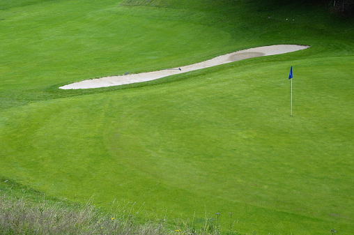 Part of golf course with blue flag and hole in green lawn