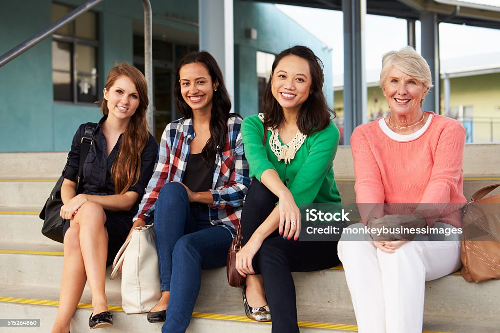 Four female teachers sitting on steps at entrance of school Teacher Stock Photo