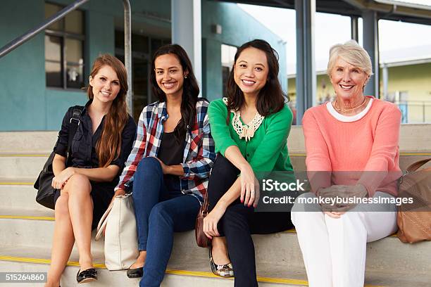 Four Female Teachers Sitting On Steps At Entrance Of School Stock Photo - Download Image Now