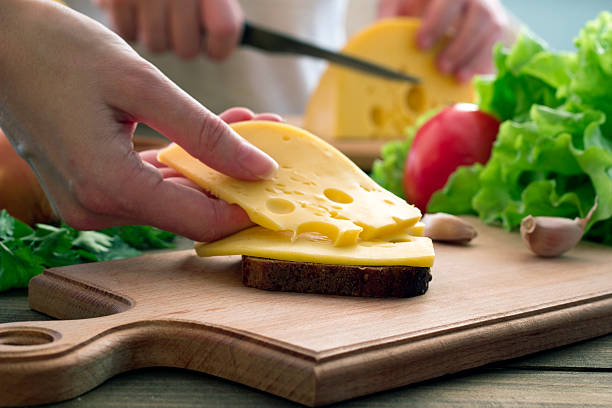 Hand lays down a piece of cheese on bread Hand lays down a piece of cheese on bread and vegetables sandwich new hampshire stock pictures, royalty-free photos & images