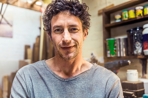 A photo of confident worker. Portrait of a mature male is smiling in workshop. Handsome man is in casuals at repair shop.