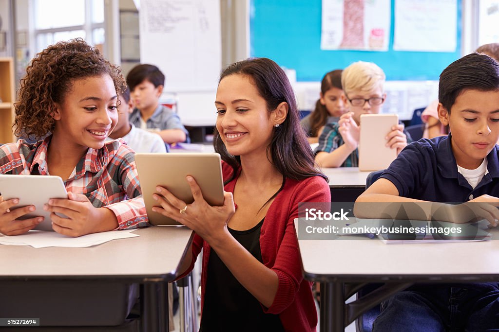 Teacher helping kids with computers in elementary school Teacher Stock Photo